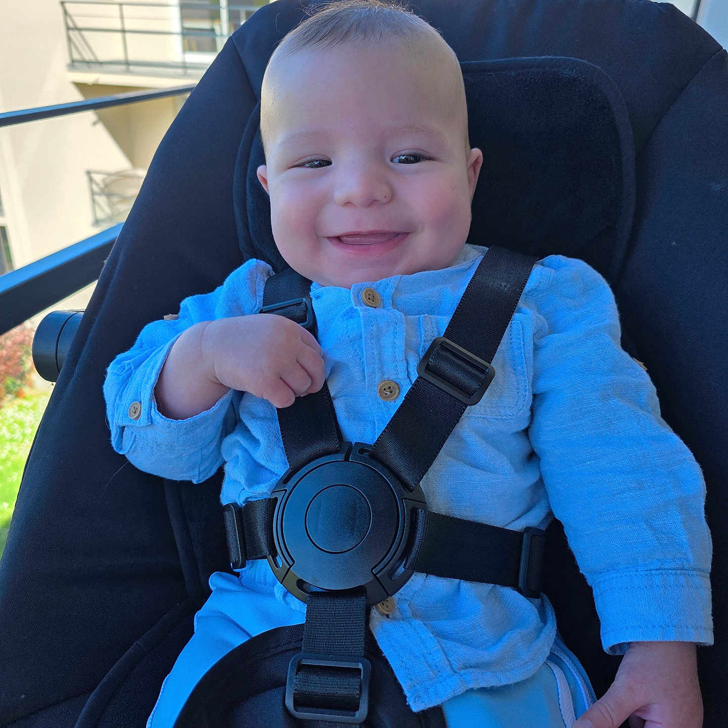 Ethan a rejoint le concours — aidez-le/la à gagner de superbes lots ! baby, child, smile, stroller, blue_clothing, button_up_shirt, safety_harness, outdoor, daylight, modern_building, greenery, happy, face, person, infant, seated, cute, expression, hand, casual_wear