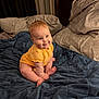baby, child, yellow_onesie, blue_blanket, bed, pillow, smile, cute, indoors, soft_lighting, chubby_cheeks, sitting, infant, warm_colors, cozy, happy, portrait, person, furniture, blanket