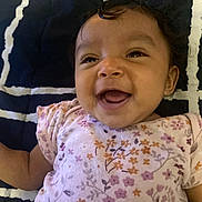 Jamaria is registered to the contest to win money with this photo: baby, smiling, infant, child, floral_clothing, blanket, patterned_blanket, happy, cute, portrait, face, lying_down, indoor, young_child, person, head, skin, eyes, mouth, expression