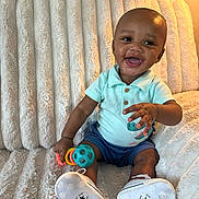 Mateo is registered to the contest to win money with this photo: baby, child, smiling, sitting, toy, couch, plush, clothing, shorts, shirt, footwear, happy, indoor, portrait, face, hand, infant, cute, playful, home