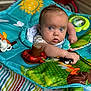 Elias is registered to the contest to win money with this photo: baby, infant, play_mat, toy, colorful, blue_eyes, curious, child, indoor, striped_blanket, cute, small_arm, patterned_clothing, soft_toys, red_toy_car, bright_colors, face, expression, young, playtime