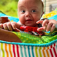 Elias is registered to the contest to win money with this photo: baby, child, infant, toy, play_mat, colorful, striped, hand, face, blue_eyes, closeup, indoor, curious, smiling, crawling, bright, patterned, soft_toys, person, young