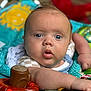 baby, infant, face, blue_eyes, arm, toys, playmat, colorful, polka_dots, sun_design, close_up, expression, child, skin, clothing, indoor, cute, person, focus, reaching