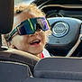 car, casual, child, curly_hair, daylight, fun, happy, inside, jeep, portrait, reflection, seat, smiling, steering_wheel, sunglasses, sunlight, transportation, vehicle_interior, window, young