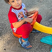 Mateo joined the competition — help win amazing prizes! blue_sandals, casual, child, concrete, curly_hair, cute, grass, looking_up, outdoor, pajamas, plastic_toy, play, playtime, red_clothing, sandals, smiling, summer, sunlight, toy_vehicle, young_child