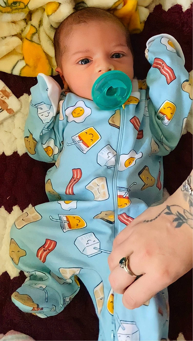 Makoa is registered to the contest to win money with this photo: arm, baby, baby_toddler_clothing, cheek, chest, child, finger, gesture, linens, mouth, nail, organ, pattern, people, person, sleeve, t_shirt, textile, toddler, white