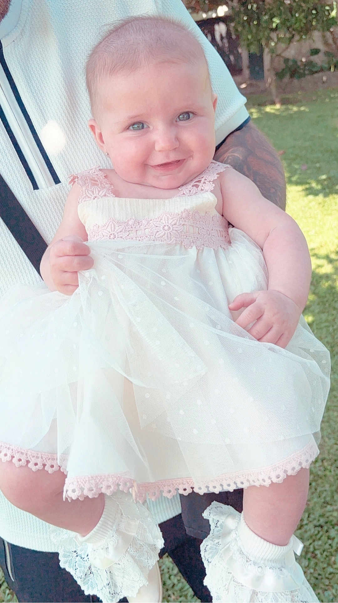 Isabella is registered to the contest to win money with this photo: baby, child, smile, dress, white_dress, lace, outdoor, sunlight, grass, person, holding, cute, happy, footwear, socks, garden, portrait, infant, young_child, human