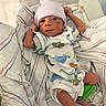newborn, baby, infant, child, hospital, bassinet, blanket, swaddle, hat, beanie, onesie, dinosaur, clothing, portrait, lying_down, face, eyes_open, arms, legs, indoor