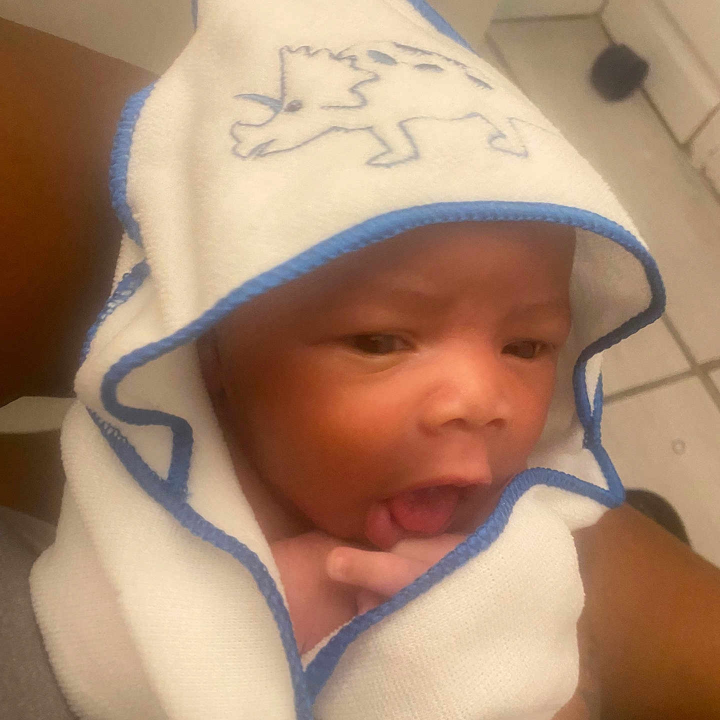 Jarez is registered to the contest to win money with this photo: arm, baby, child, cute, dinosaur, expression, face, floor, hand, holding, hooded_towel, indoor, infant, newborn, person, skin, soft, tile, tongue, towel