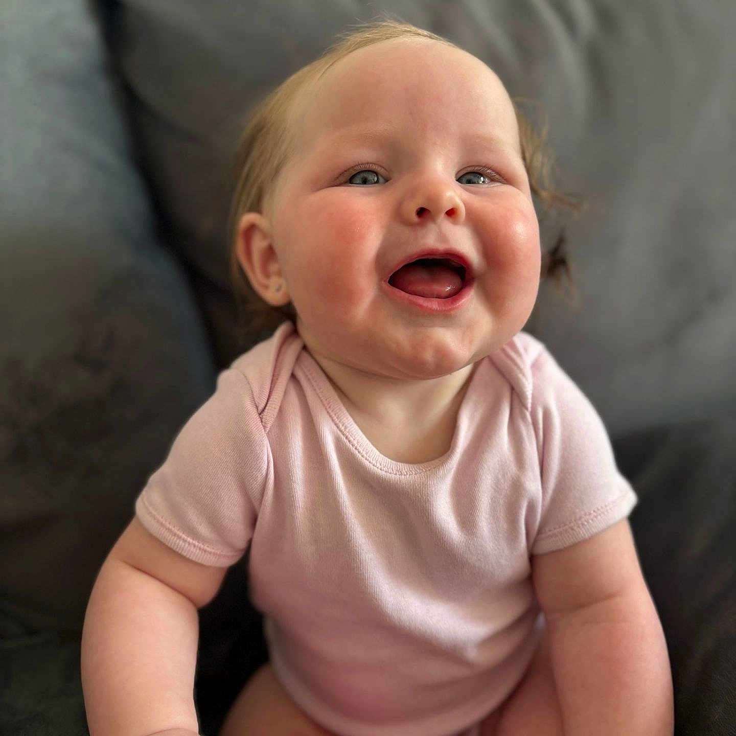 Ivy-Lou joined the competition — help win amazing prizes! baby, child, chubby_cheeks, couch, cute, expression, face, hand, happy, indoor, infant, person, pink_onesie, portrait, remote_control, sitting, skin, smiling, toy, young_child