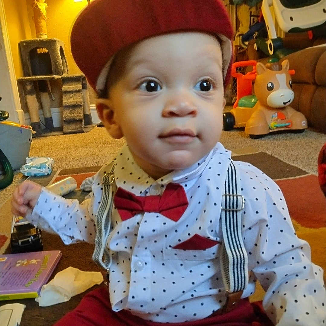 Jaxxon is registered to the contest to win money with this photo: baby, book, bow_tie, cap, carpet, child, clothing, curious, cute, furniture, indoor, lamp, living_room, polka_dot, portrait, sitting, smiling, suspenders, toddler, toy