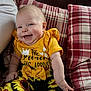 baby, child, smiling, yellow_clothing, sunflower_pattern, cushion, plaid, red, indoor, happy, cute, infant, person, seated, portrait, head, face, arm, bow, fabric