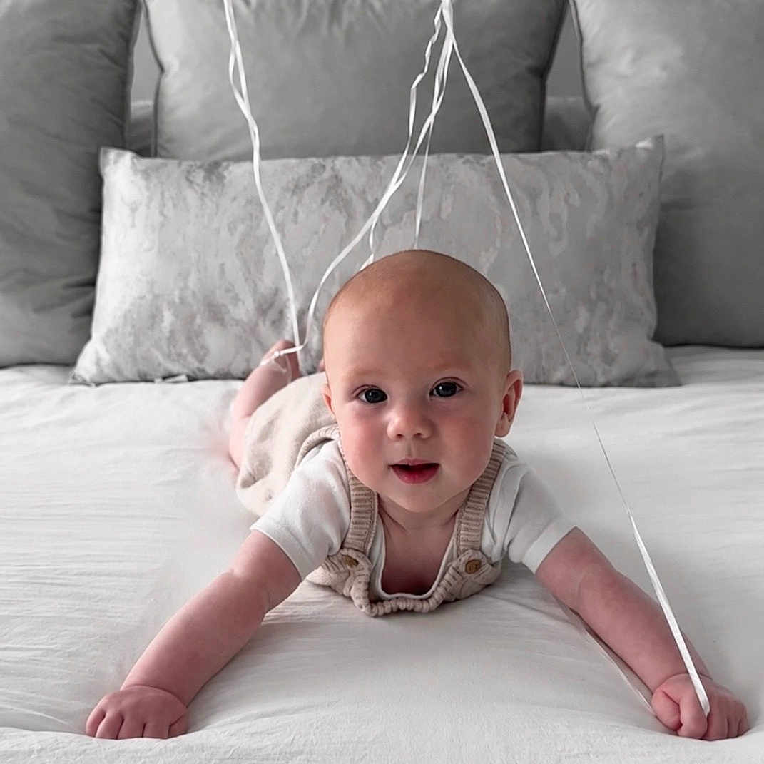 Austen joined the competition — help win amazing prizes! baby, infant, balloons, bed, white_bed, pillow, gray_pillow, smiling, cute, child, indoor, person, portrait, crawling, holding, celebration, happy, home, soft_lighting, cozy