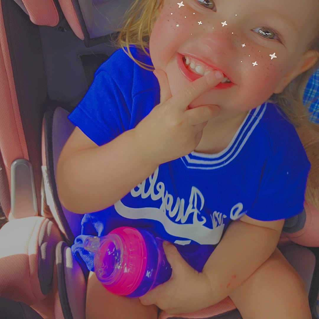 Everleigh is registered to the contest to win money with this photo: baby, bodypart, car, car_interior, carseat, clothing, cushion, face, finger, hand, happy, head, homedecor, person, photography, portrait, shorts, sitting, smile, t_shirt