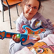 Younala a rejoint le concours — aidez-le/la à gagner de superbes lots ! blanket, cartoon_character, casual_clothing, chair, child, cute, floor, girl, glasses, happy, hoodie, indoor, person, play, room, smiling, toy_guitar, unicorn, wood_floor, wooden_furniture