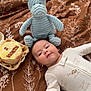 Soren is registered to the contest to win money with this photo: baby, infant, plush_toy, moose, bedspread, floral_pattern, cake, celebration, milestone, smiling, lying_down, white_outfit, cute, soft_toy, indoor, child, young_baby, sleepwear, face, happy