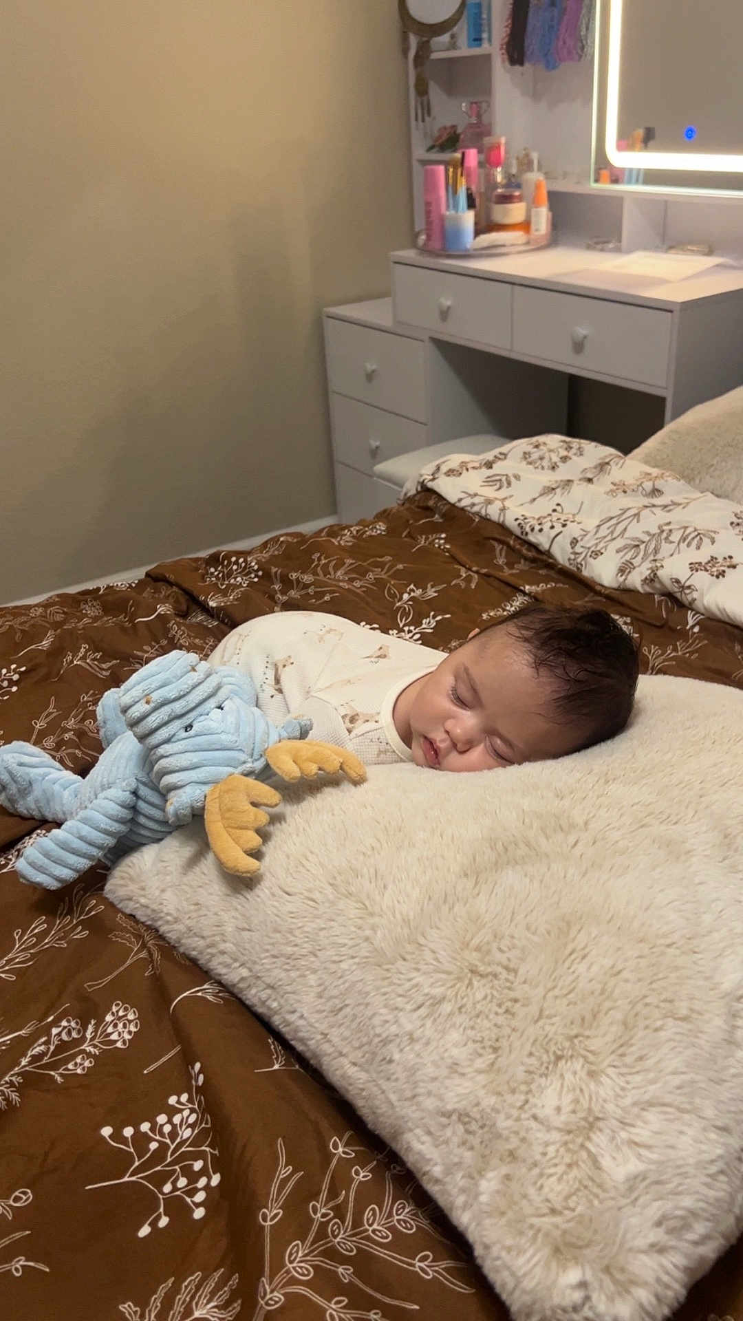 Soren is registered to the contest to win money with this photo: baby, sleeping, plush_toy, bed, pillow, blanket, brown, cream, soft, cozy, nursery, vanity, mirror, skincare, beauty_products, furniture, indoors, child, peaceful, cute