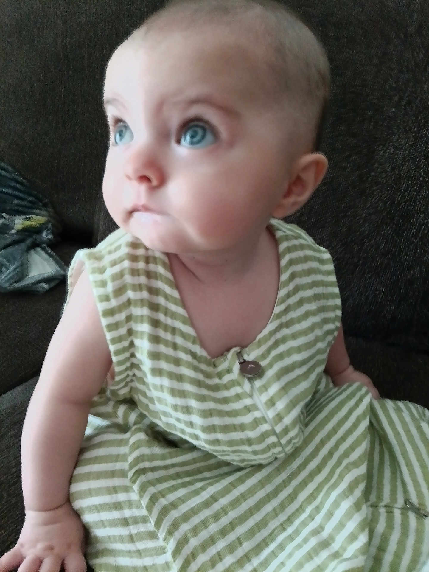 Ellie is registered to the contest to win money with this photo: baby, child, blue_eyes, striped_clothing, sitting, couch, indoor, curious, face, head, arm, skin, infant, young_child, portrait, person, clothing, button, closeup, expression