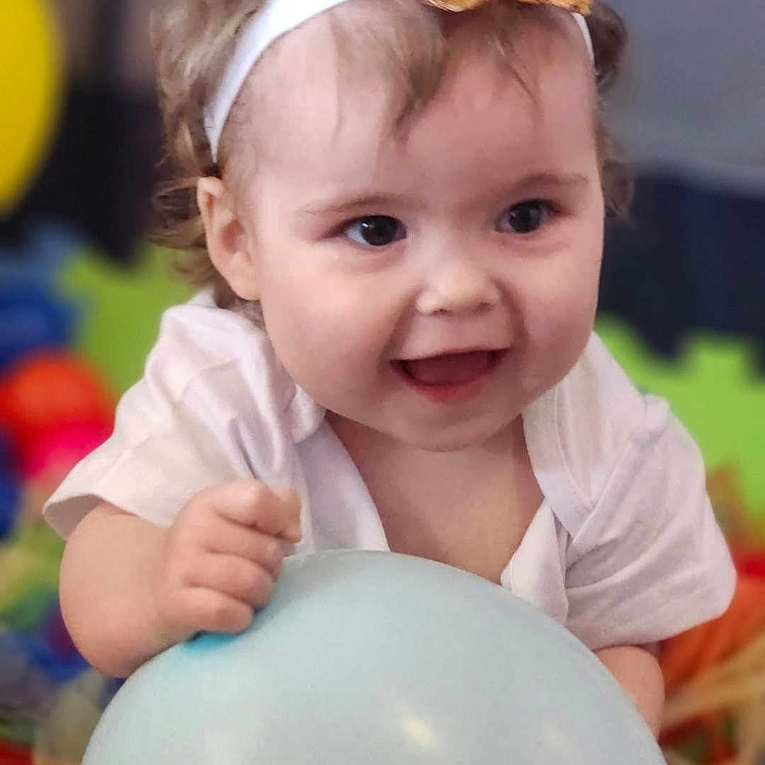 Isabella is registered to the contest to win money with this photo: baby, balloon, cheerful, child, clothing, colorful, cute, face, hand, happy, headband, indoor, infant, playmat, playtime, portrait, seated, smiling, toy, young_child