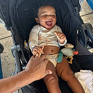 Kamari joined the competition — help win amazing prizes! baby, child, smiling, laughing, stroller, hand, curly_hair, toy, blanket, outdoor, happy, infant, skin, clothing, person, seat, comfort, playful, cute, joyful