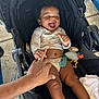 baby, child, smiling, laughing, stroller, hand, curly_hair, toy, blanket, outdoor, happy, infant, skin, clothing, person, seat, comfort, playful, cute, joyful