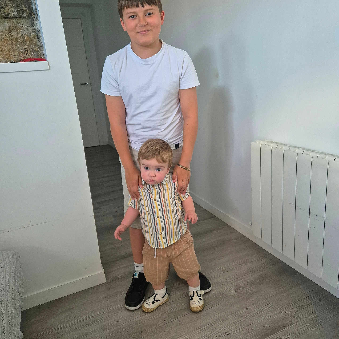 Vasile a rejoint le concours — aidez-le/la à gagner de superbes lots ! bracelet, casual_clothing, child, curious, door, floor, flooring, hair, holding, home, indoor, radiator, shoes, shorts, smile, socks, standing, striped_shirt, toddler, white_wall