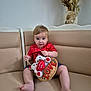 baby, barefoot, basket, child, couch, decor, dried_plants, expression, face, furniture, indoor, love, person, red_shirt, seated, sofa, teddy_bear, toddler, toy, vase