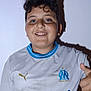 child, boy, smile, thumbs_up, curly_hair, white_shirt, sports_jersey, indoor, portrait, happy, blue_eyes, shadow, wall, short_sleeves, casual, person, young, front_view, standing, positive_gesture