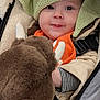 baby, child, face, knitted_hat, green_hat, stuffed_animal, buffalo_plush, orange_bib, striped_sleeve, stroller, cozy_clothing, warm_fabric, cute_expression, indoor, portrait, smiling, soft_toys, infant, closeup, winter_wear
