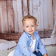 Wahid a rejoint le concours — aidez-le/la à gagner de superbes lots ! blue_eyes, blue_shirt, boy, bracelet, casual_clothing, child, cozy, curly_hair, cushion, cute, fluffy, happy, indoor, jeans, portrait, sitting, smile, white_tshirt, wooden_background, young