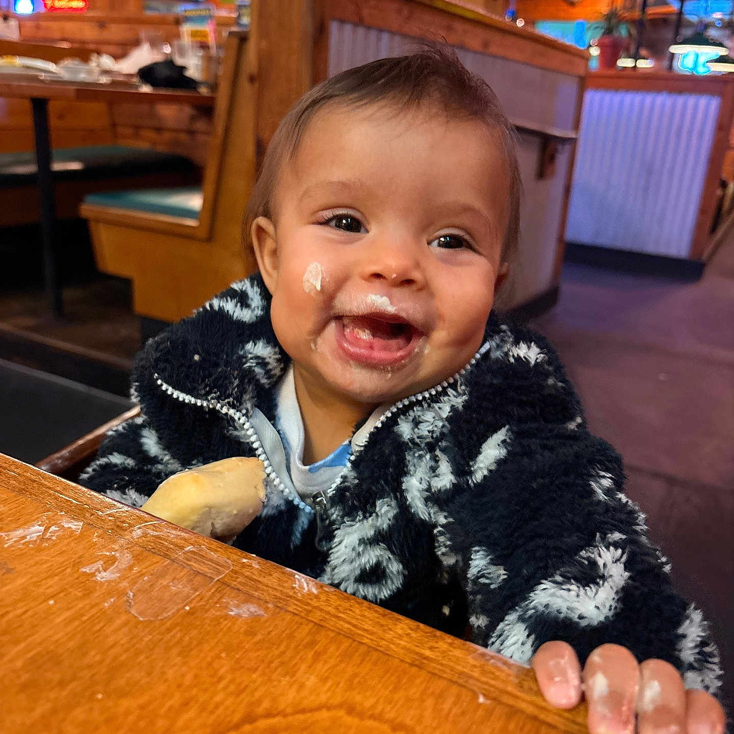 Xiomora is registered to the contest to win money with this photo: baby, booth, bread, candid_photo, child, cute, dining, face, food, fuzzy_jacket, hands, happy, high_emotion, infant, messy_face, portrait, restaurant, seat, smiling, wooden_table