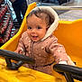baby, infant, child, shopping_cart, yellow_cart, steering_wheel, pink_jacket, hood, smile, happy, grocery_store, supermarket, shelves, bread, person, candid, portrait, winter_clothing, seat, hands