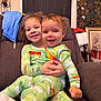 child, baby, children, siblings, matching_pajamas, green_pajamas, smile, happy, couch, sofa, indoor, living_room, portrait, family, hug, hands, curly_hair, infant, playful, cozy