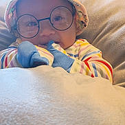 Zachariah joined the competition — help win amazing prizes! baby, glasses, hat, blanket, striped_clothing, couch, indoor, child, face, cute, cozy, person, portrait, apparel, headwear, smile, soft_texture, sitting, baby_gloves, colorful
