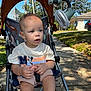 Asa is registered to the contest to win money with this photo: toddler, stroller, child, outdoor, sunny, sidewalk, fan, mickey_mouse, shirt, shorts, grass, tree, house, car, shade, hand, legs, curious, baby, summer