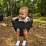 Asa joined the competition — help win amazing prizes! toddler, child, swing, playground, outdoor, trees, wood_chips, baby, greenery, sunlight, park, play, seat, clothing, socks, nature, daytime, person, expression, curious