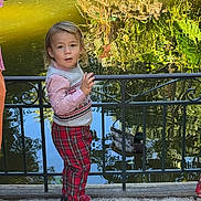 Nathan a rejoint le concours — aidez-le/la à gagner de superbes lots ! casual_clothing, child, curly_hair, daytime, duck, fence, greenery, nature, outdoor, person, pond, red_pants, reflection, shoes, standing, stone_path, sunlight, toddler, vest, water