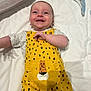 Jackson is registered to the contest to win money with this photo: baby, smiling, yellow_overalls, leopard_print, infant, happy, lying_down, white_bed, cute, child, clothing, portrait, indoor, face, person, baby_girl, baby_boy, soft_light, joy, small_child
