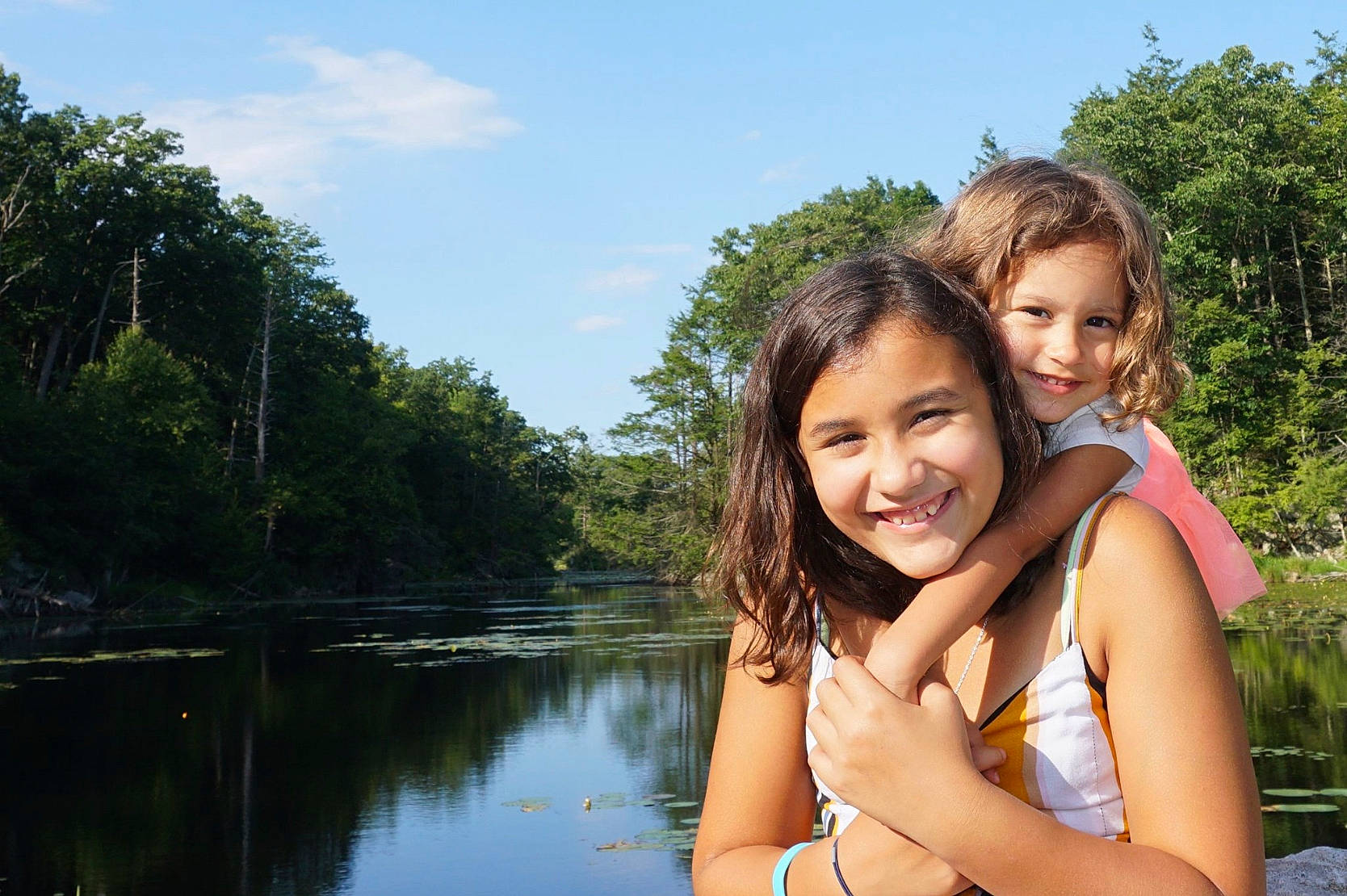 Jasmyne is registered to the contest to win money with this photo: bank, beauty, botany, child, facial_expression, friendship, fun, grass, happy, joy, lake, leisure, long_hair, people_in_nature, person, photography, river, smile, summer, tree