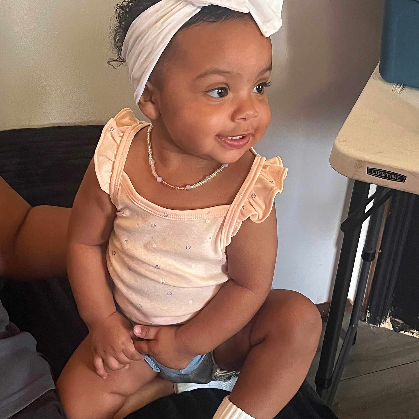Mia Carolina is registered to the contest to win money with this photo: black_surface, casual, child, curly_hair, cute, furniture, happy, headband, home, indoors, necklace, person, shorts, sitting, skin_tone, smiling, socks, table, toddler, white_bow