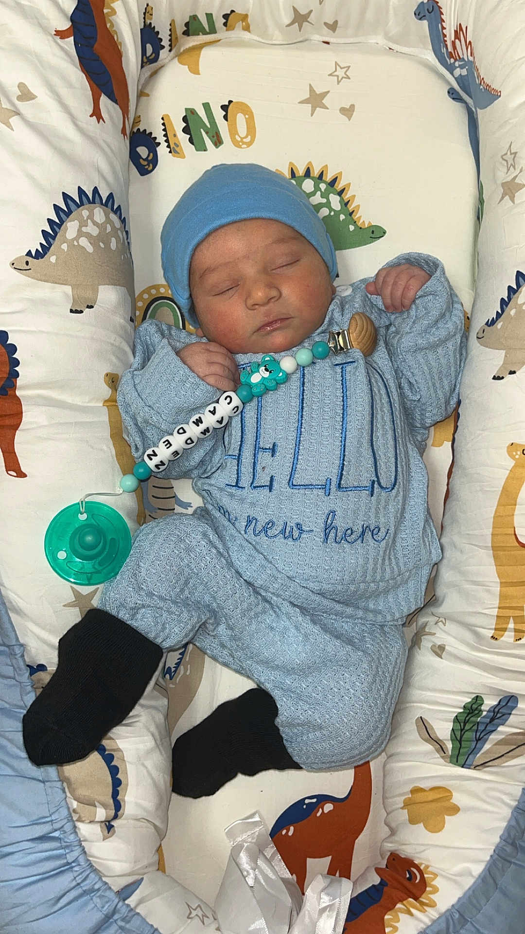 Camden joined the competition — help win amazing prizes! baby, newborn, sleeping, blue_outfit, hat, pacifier, beads, cushion, dinosaur_pattern, infant, cozy, child, soft_toys, crib, black_socks, cute, resting, indoors, peaceful, clothing