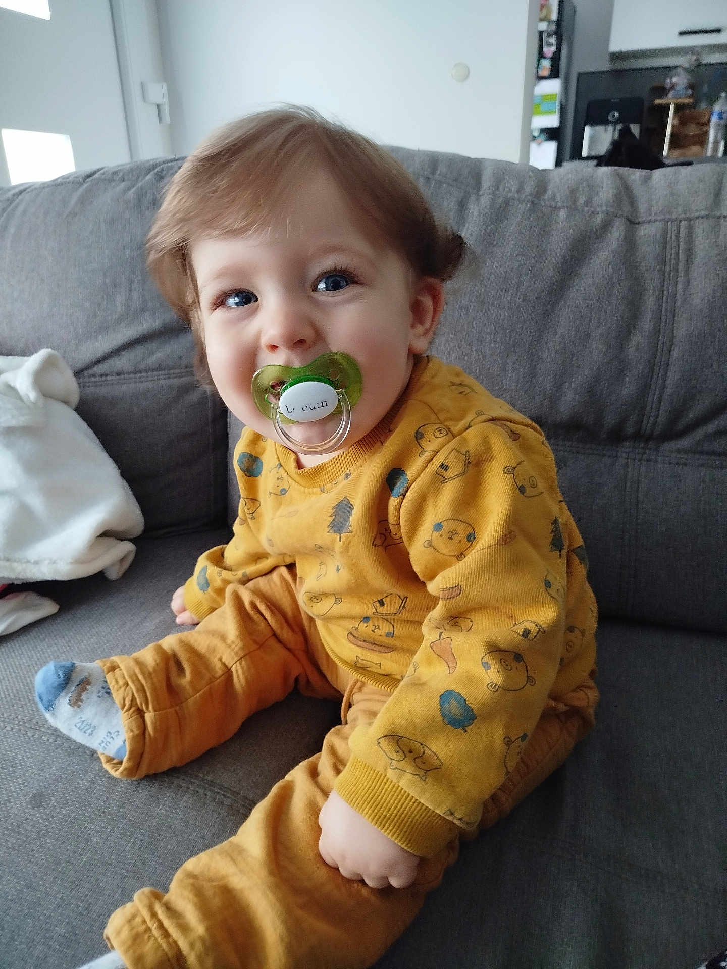 Charly participe au concours pour gagner de l'argent avec cette photo : toddler, child, pacifier, sitting, couch, indoors, yellow_clothing, cozy, cute, happy, face, hair, sock, home, furniture, patterned_clothing, baby, comfort, person, portrait