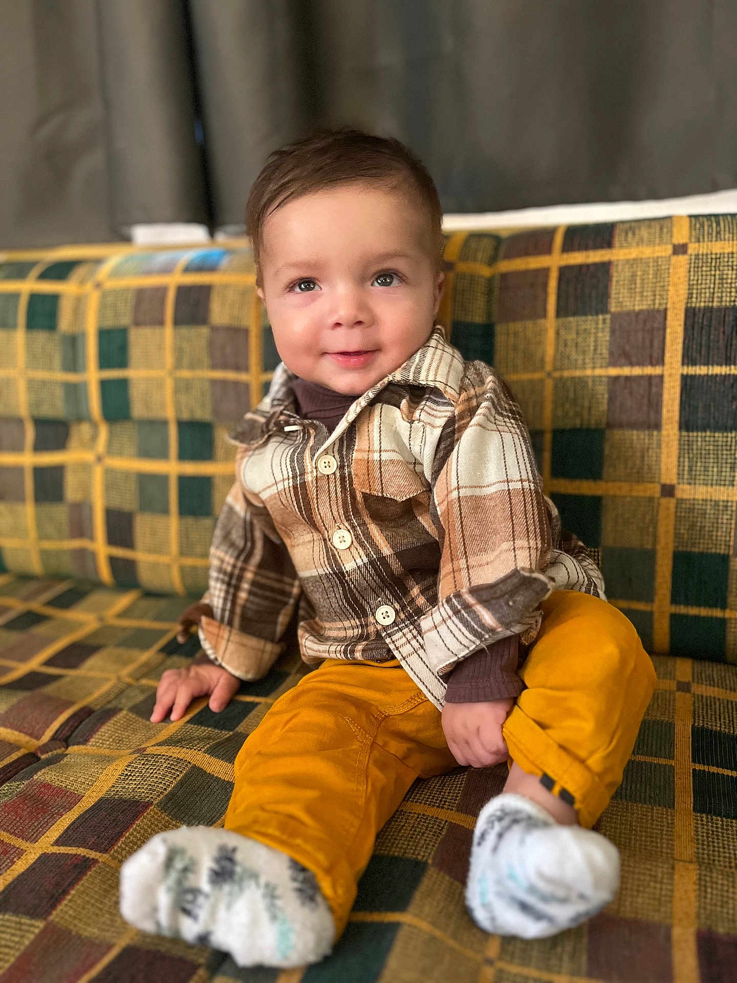 Simon a rejoint le concours — aidez-le/la à gagner de superbes lots ! toddler, child, smiling, plaid_shirt, mustard_pants, socks, couch, patterned_fabric, indoor, portrait, cute, happy, seated, young_child, cozy, casual_clothing, curly_hair, colorful, home, playful