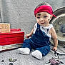 baby, child, overalls, red_headband, tools, wrench, keys, nuts_and_bolts, wooden_blocks, months, grease_smudges, denim, white_socks, sitting, gray_background, metal_parts, cute, portrait, indoors, hands