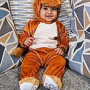 Dhriti is registered to the contest to win money with this photo: baby, child, costume, couch, cozy, cute, footwear, happy, headgear, indoors, lion_costume, patterned_pillows, pillows, plush, portrait, seated, small_hands, smiling, soft_texture, warm_colors