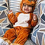 baby, child, lion_costume, smile, couch, pillow, pattern, plush, happy, cute, indoors, cozy, infant, footwear, soft, fabric, sitting, headgear, person, portrait
