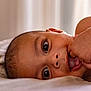 baby, close_up, face, hand, fingers, curious, lying_down, skin, eyes, infant, portrait, soft_light, expression, child, mouth, tongue, indoors, natural_light, young, cute
