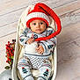 baby, infant, holiday_clothing, santa_hat, knitwear, basket, pom_pom, silver_ornament, red_berries, wooden_floor, festive, cozy, cute, child, portrait, indoors, smiling, christmas_theme, holiday, person