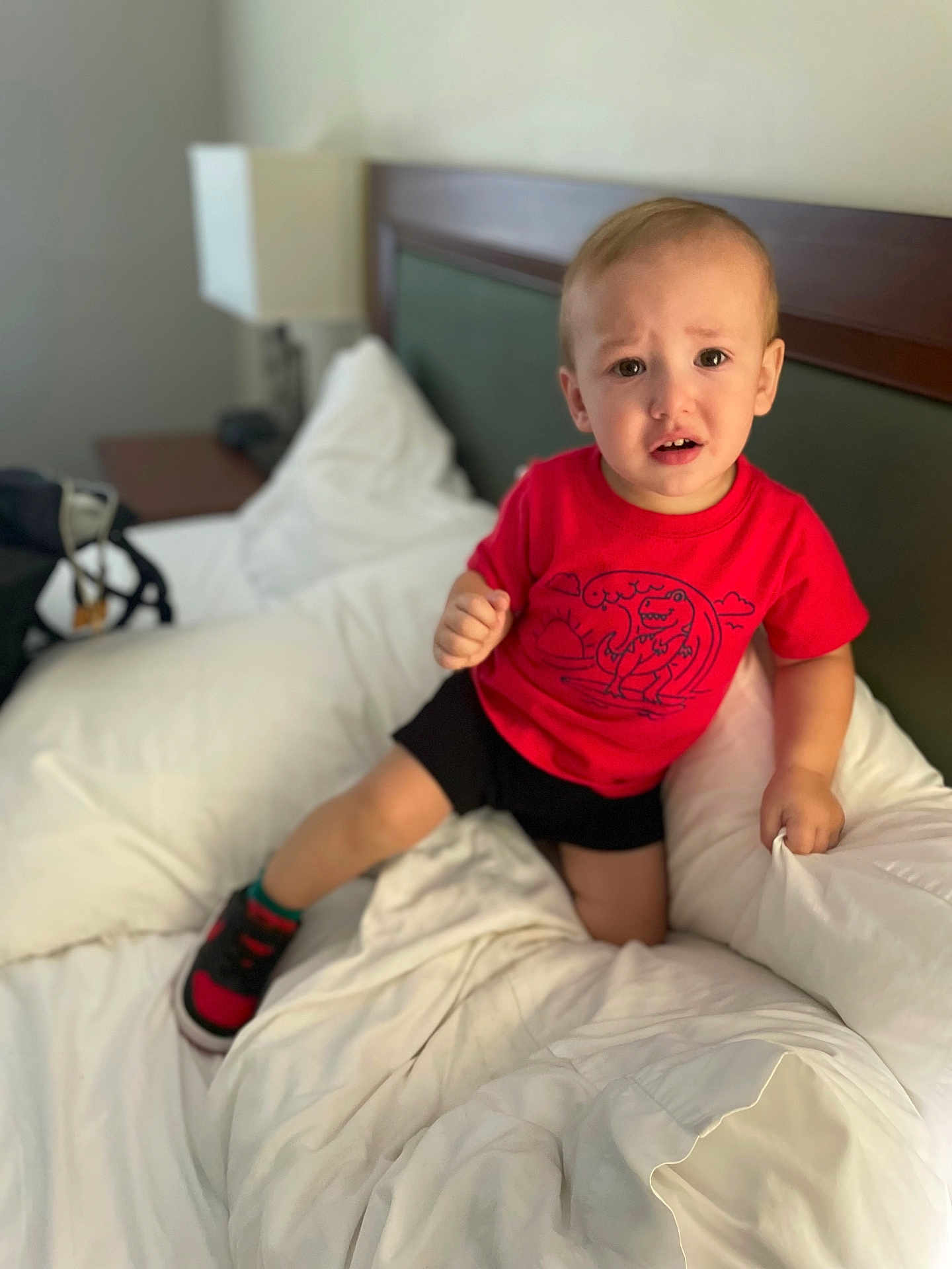 Othrin joined the competition — help win amazing prizes! toddler, child, bed, white_bedding, red_tshirt, dinosaur_print, black_shorts, shoe, indoor, lamp, headboard, furniture, confused_expression, person, young_child, room, blanket, pillow, footwear, casual_clothing