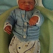 Ilyan a rejoint le concours — aidez-le/la à gagner de superbes lots ! newborn, baby, sleeping, knitted_clothing, blue_sweater, white_pants, patterned_pants, blanket, soft, cozy, infant, cute, resting, child, small_hands, headwear, warm, indoors, portrait, peaceful